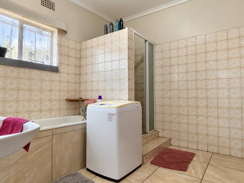 A functional bathroom featuring a built-in bathtub, separate shower enclosure, and pedestal washbasin, finished with dated ceramic wall and floor tiles.