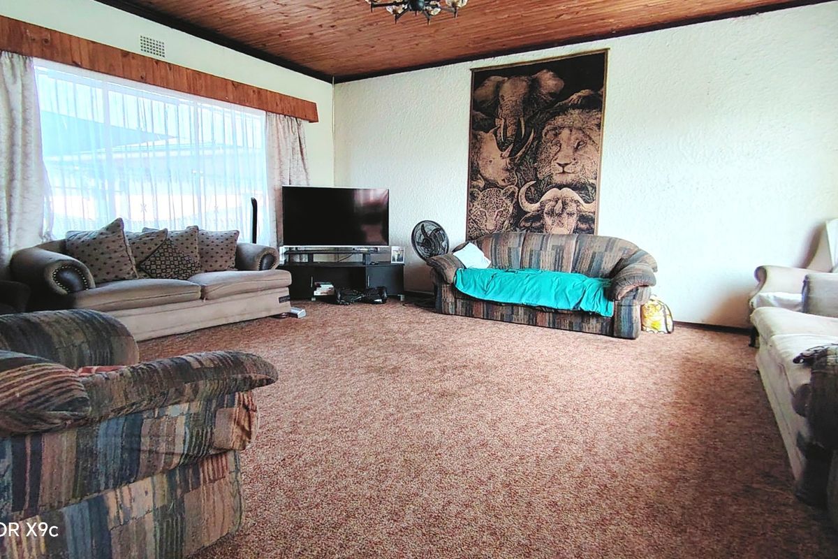 Spacious living room featuring a timber-clad ceiling, large window for natural light, and carpeted flooring, offering a dated but functional layout.
