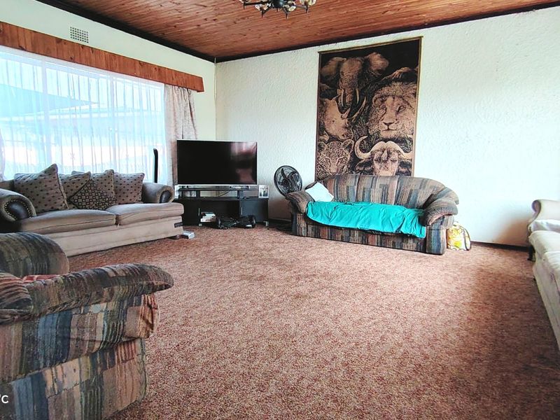 Spacious living room featuring a timber-clad ceiling, large window for natural light, and carpeted flooring, offering a dated but functional layout.