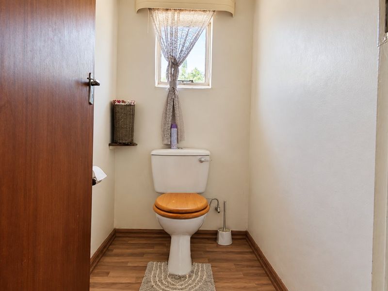 A compact bathroom featuring a standard toilet, laminate flooring, and a small window providing natural light.
