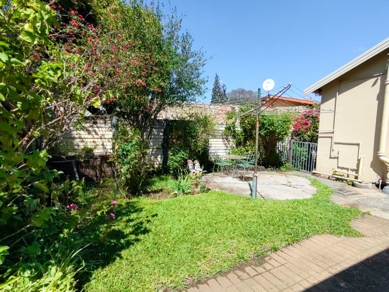 A rear garden area featuring a paved patio, established lawn, boundary wall, and a rotary clothesline, offering a private outdoor space.