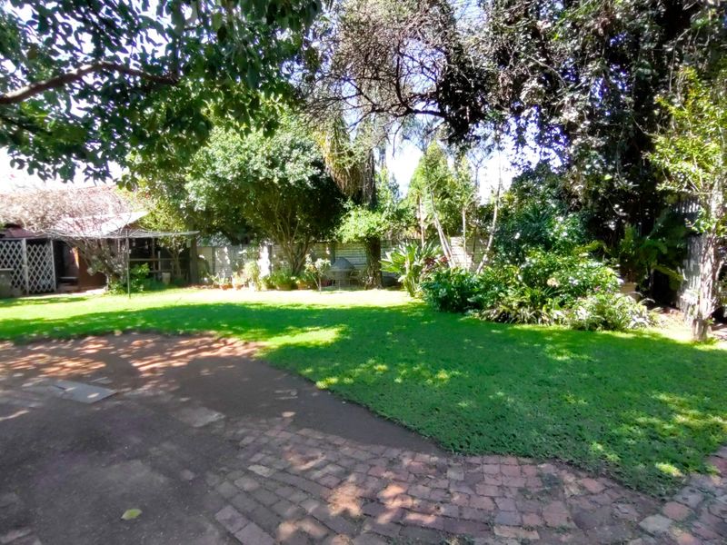 A spacious, well-established garden featuring mature trees, lush lawn, and brick-paved pathways, offering a private and tranquil outdoor setting.