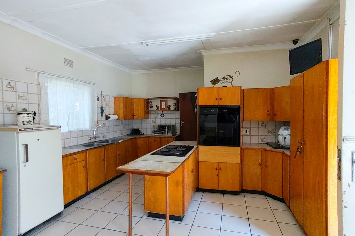 A dated kitchen featuring wooden cabinetry, a central island with a gas hob, built-in oven, and tiled flooring throughout.