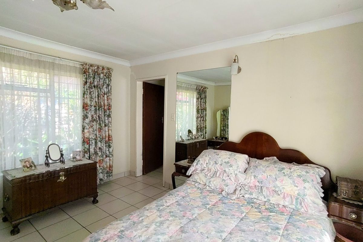 A bedroom featuring tiled flooring, a built-in wall mirror, and coved ceilings. The space shows signs of wear and requires cosmetic updates.