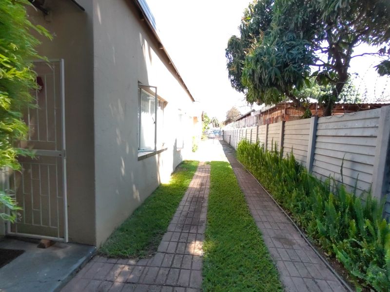 A side exterior view showing a paved driveway, landscaped garden strip, and a secure precast concrete boundary wall.