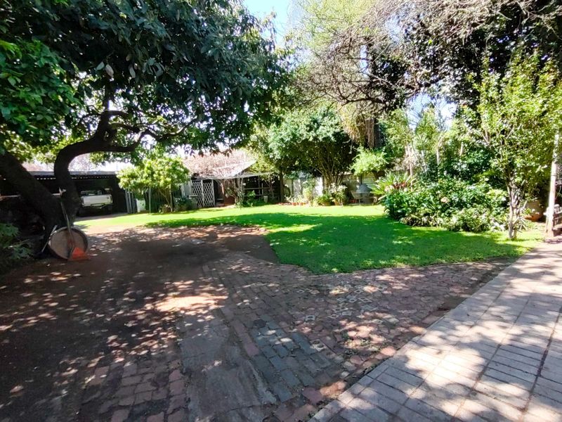 A spacious garden area featuring mature trees, a well-maintained lawn, and extensive brick paving, providing a natural outdoor setting.