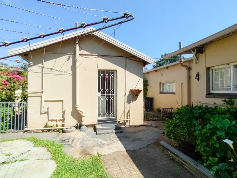 Rear exterior view of the property featuring a paved courtyard area, security gate entrance, and established garden beds.