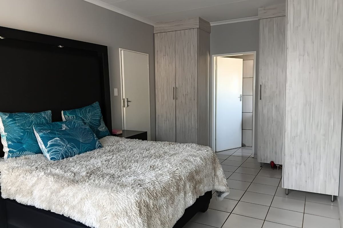 A well-maintained bedroom featuring neutral grey walls, light wood-grain built-in cupboards, and clean white floor tiles.