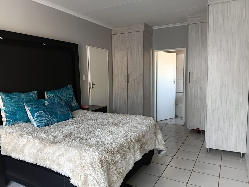 A well-maintained bedroom featuring neutral grey walls, light wood-grain built-in cupboards, and clean white floor tiles.