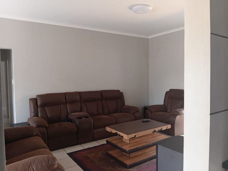 A neutrally painted living room featuring tiled flooring and a central ceiling light fixture, offering a clean and functional space.