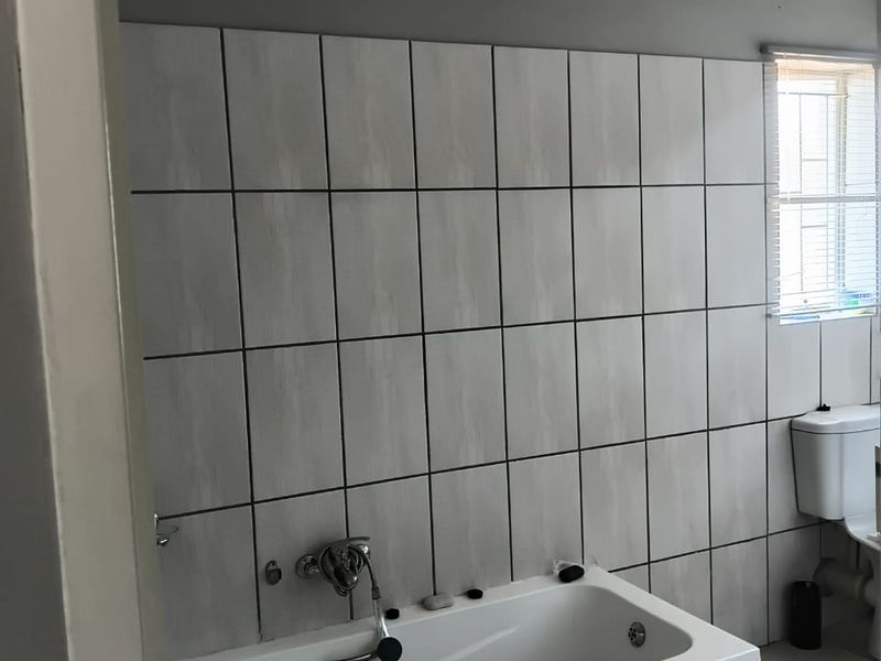 A functional bathroom featuring a built-in bathtub with wall-mounted mixer, ceramic wall and floor tiling, and a standard toilet.