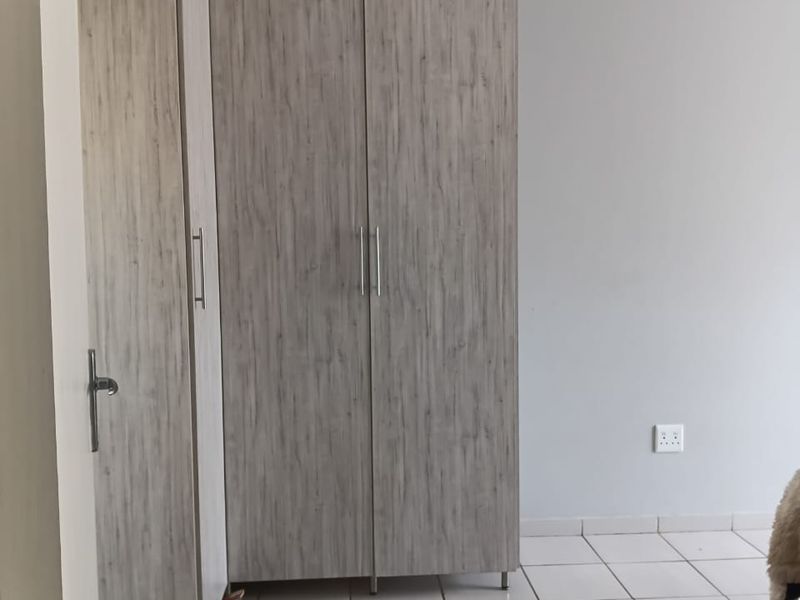 A bedroom featuring light wood-grain built-in cupboards and neutral tiled flooring, providing a clean and functional storage solution.