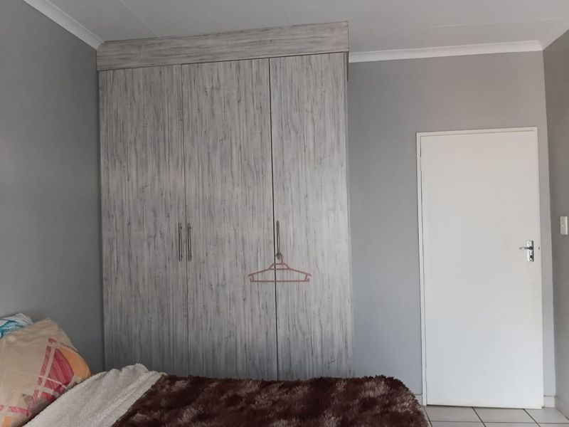 A bedroom featuring a large, light-wood grain built-in wardrobe, neutral grey walls, and tiled flooring.
