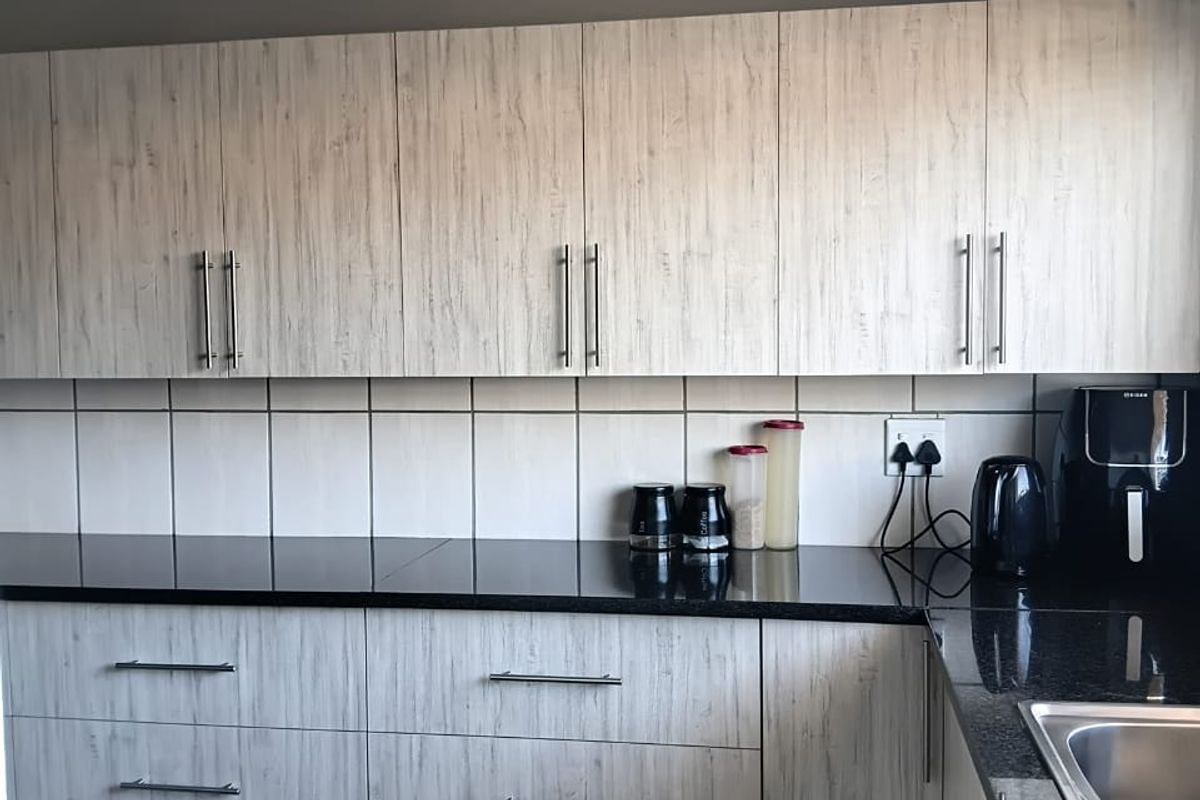 Modern kitchen featuring light wood-grain cabinetry, contrasting black granite countertops, a stainless steel sink, and clean tiled backsplash.