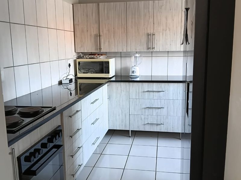 A functional kitchen featuring light wood-grain cabinetry, black granite countertops, tiled backsplash, and a built-in oven with an electric hob.