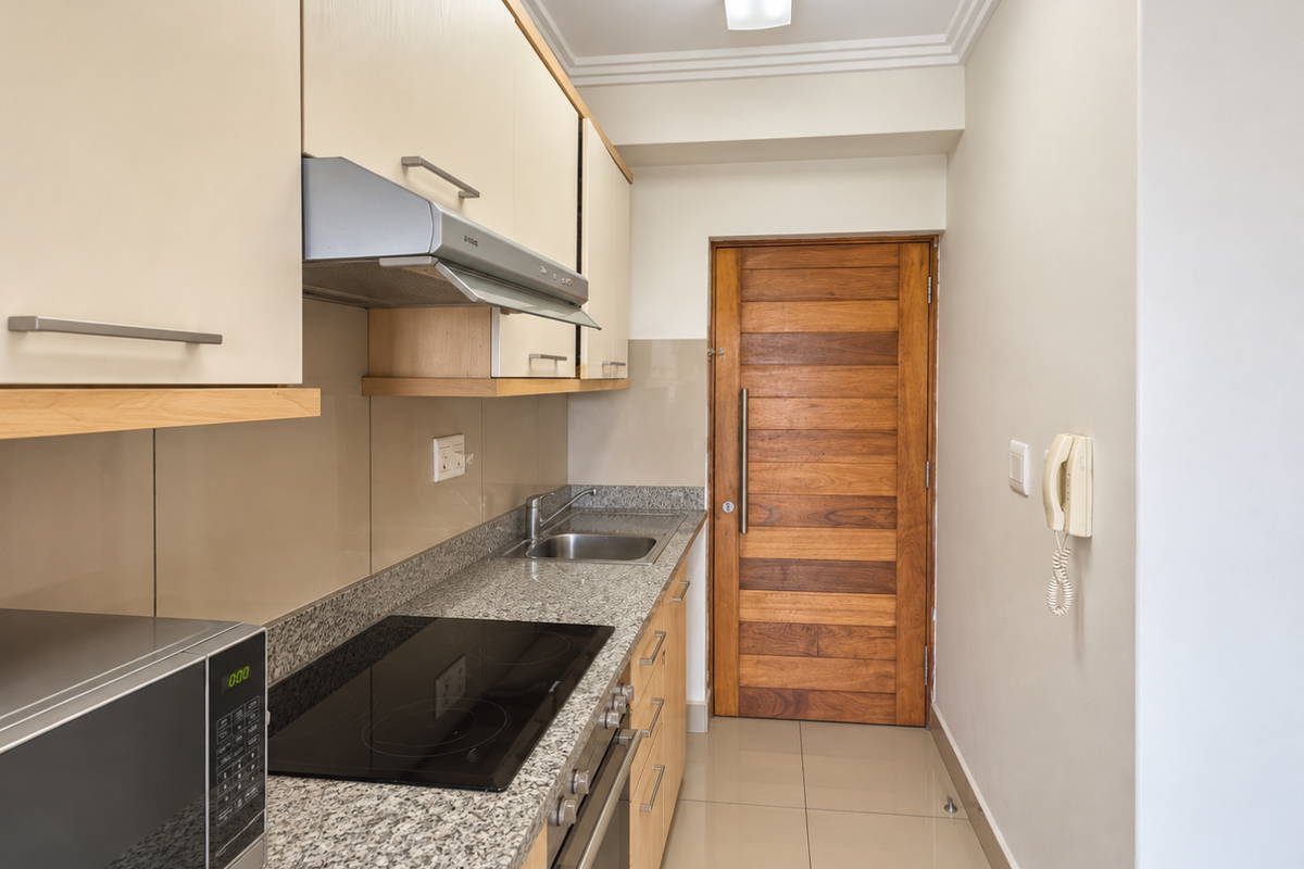A compact, well-maintained kitchen featuring granite countertops, an electric hob, built-in oven, extractor fan, and ample cabinetry with a solid wood door.