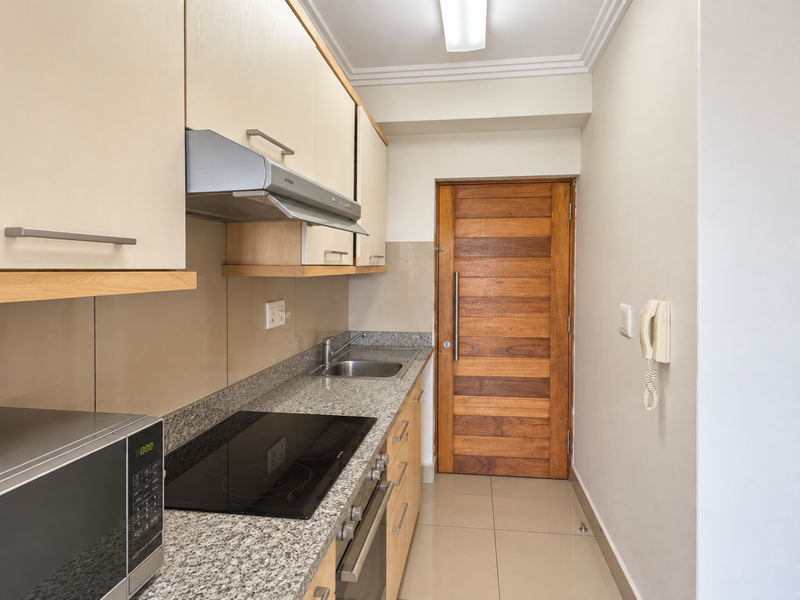 A compact, well-maintained kitchen featuring granite countertops, an electric hob, built-in oven, extractor fan, and ample cabinetry with a solid wood door.