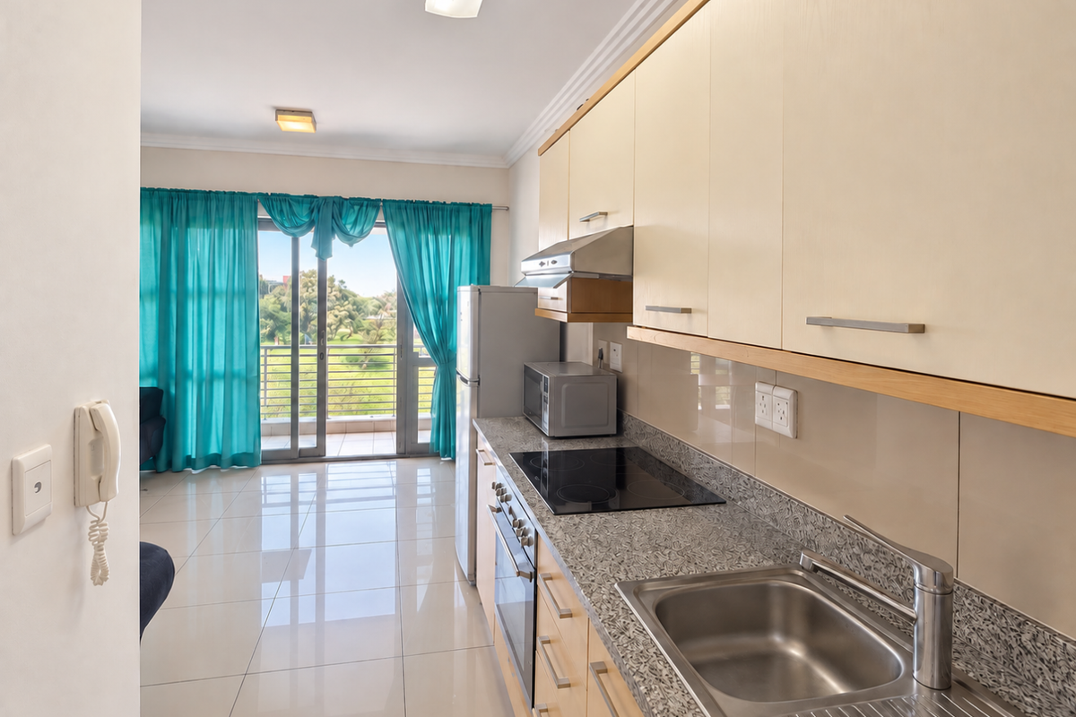 A functional kitchen featuring light wood cabinetry, granite countertops, and integrated appliances, leading directly to a balcony with natural light.