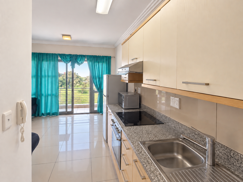 A functional kitchen featuring light wood cabinetry, granite countertops, and integrated appliances, leading directly to a balcony with natural light.