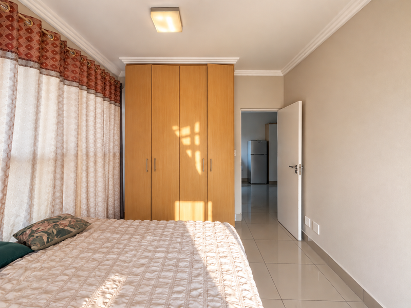 A well-maintained bedroom featuring built-in wooden wardrobes, neutral tiled flooring, and decorative ceiling cornicing, with an adjacent view into a secondary room.