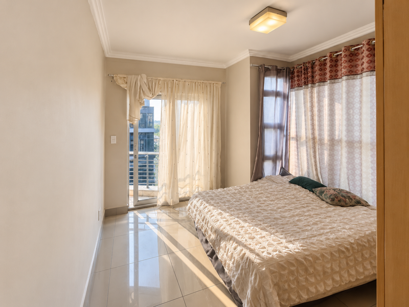 Bright bedroom featuring tiled flooring, ceiling lighting, and direct access to a private balcony through a sliding glass door.