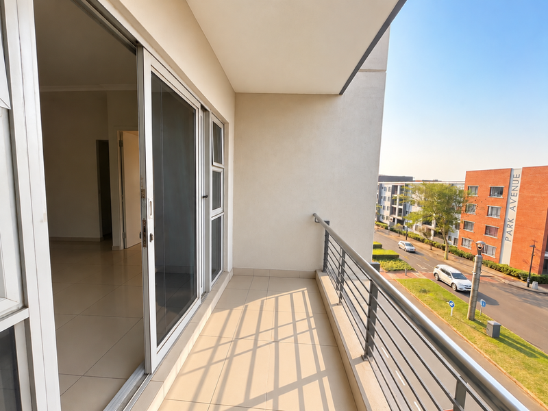 A clean, modern balcony with tiled flooring and a metal balustrade, offering an elevated view of the surrounding street and neighborhood.