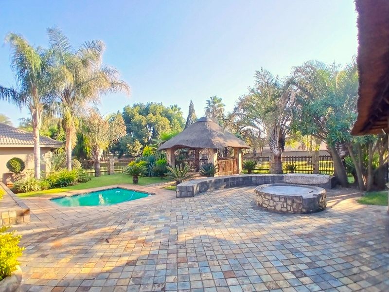 Outdoor entertainment area featuring a swimming pool, a thatched gazebo, and a stone-clad fire pit set within a paved garden space.