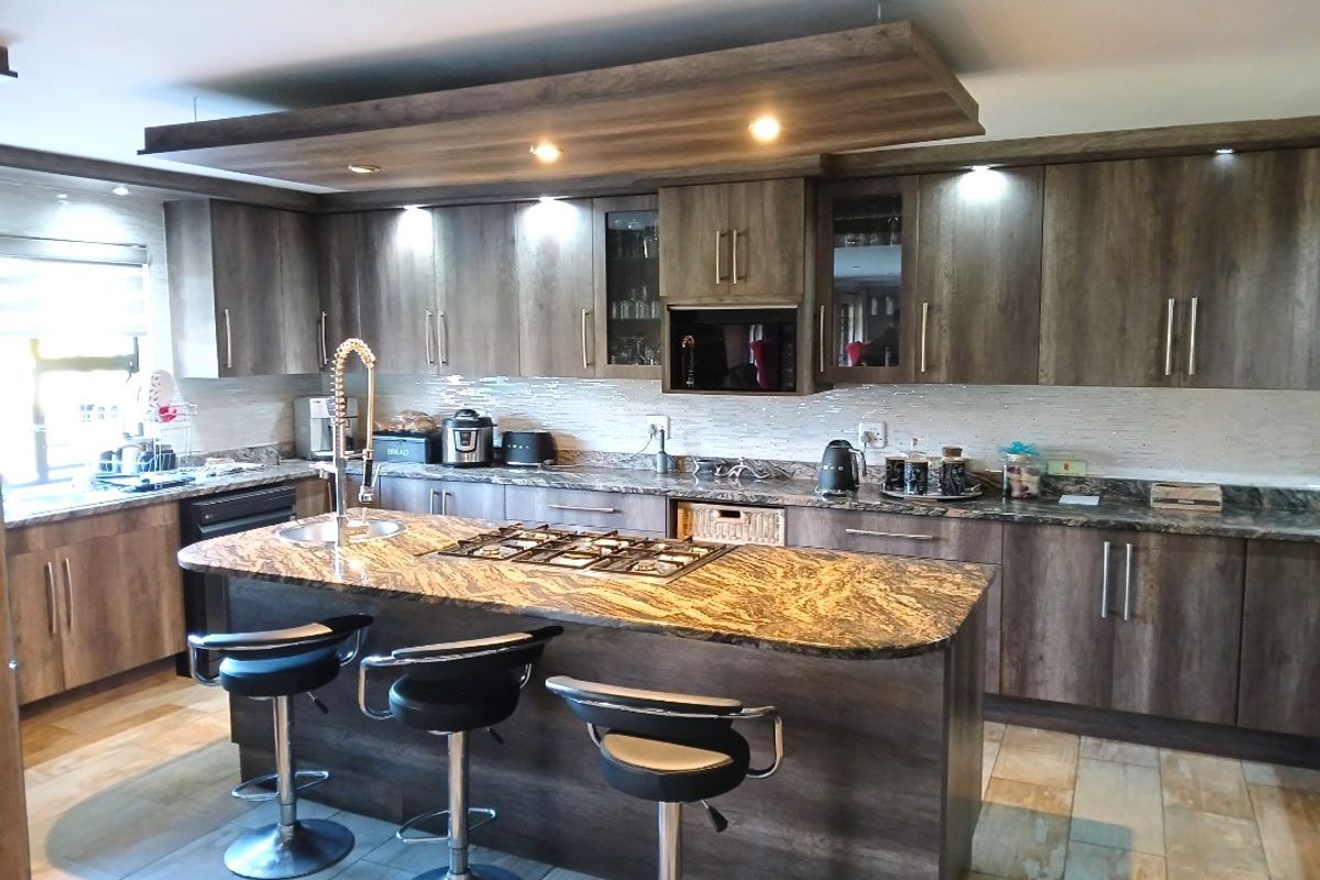 Modern kitchen featuring dark wood cabinetry, granite countertops, a central island with a gas hob, and a stylish suspended ceiling bulkhead with integrated lighting.