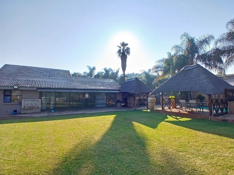 Spacious rear garden featuring a well-maintained lawn, a large tiled-roof house with sliding doors, and a traditional thatched lapa for outdoor entertainment.