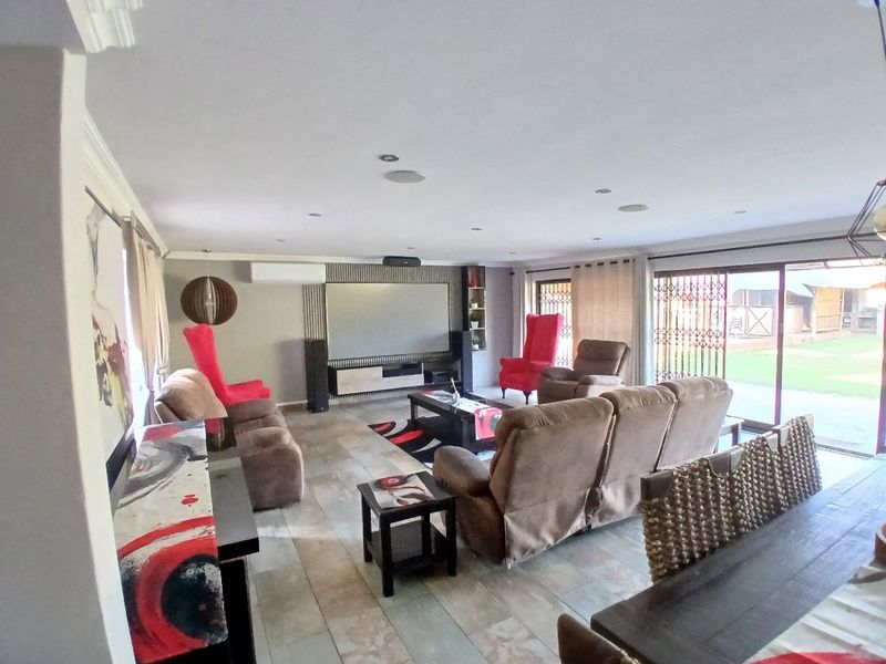Spacious living room featuring tiled flooring, recessed lighting, a built-in media wall, and large sliding glass doors providing access to the garden.