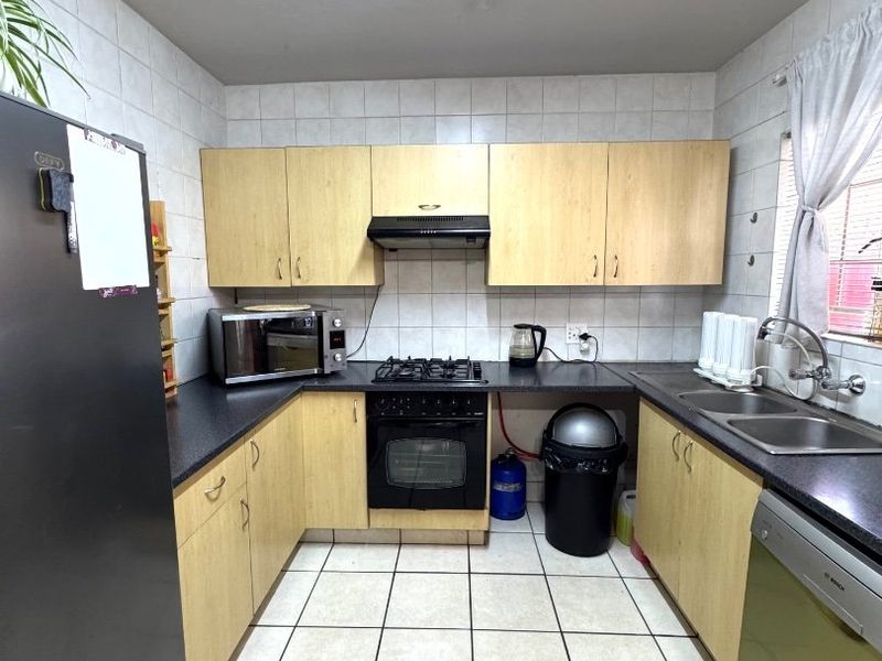 A functional kitchen featuring laminate cabinetry, a gas hob with extractor fan, double basin sink, and tiled finishes throughout.