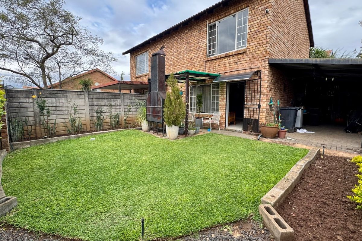 Rear view of a brick townhouse featuring a private garden, built-in braai area, and an adjacent carport.
