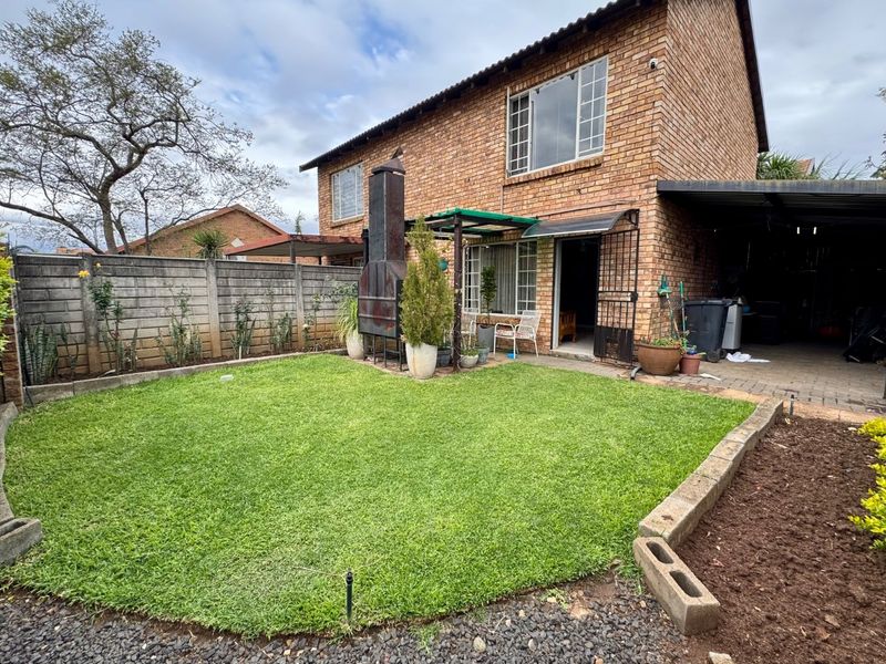 Rear view of a brick townhouse featuring a private garden, built-in braai area, and an adjacent carport.
