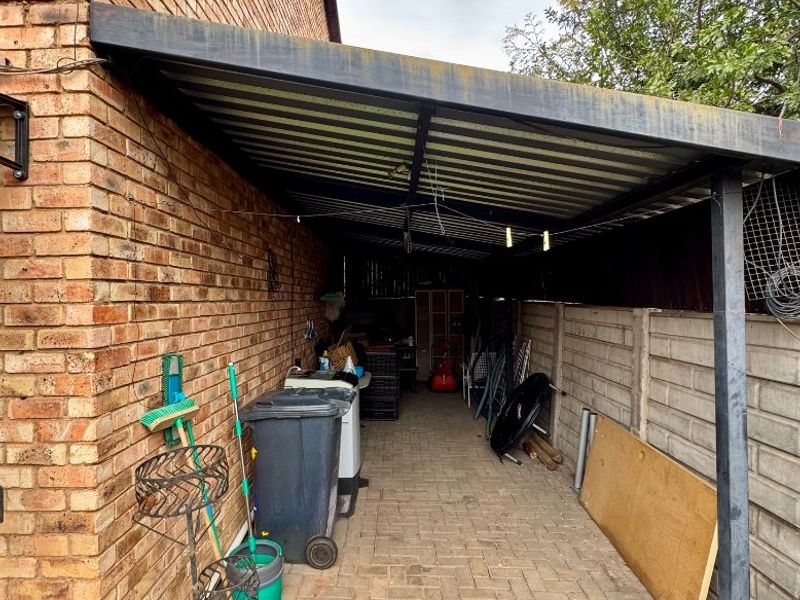 A covered side patio area featuring brick paving and a metal roof structure, providing a functional outdoor utility space.