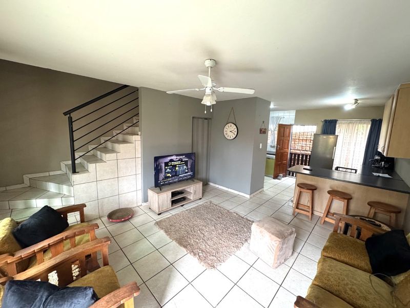 Open-plan living area featuring tiled flooring, a breakfast bar, kitchen cabinetry, and a staircase with a metal railing.