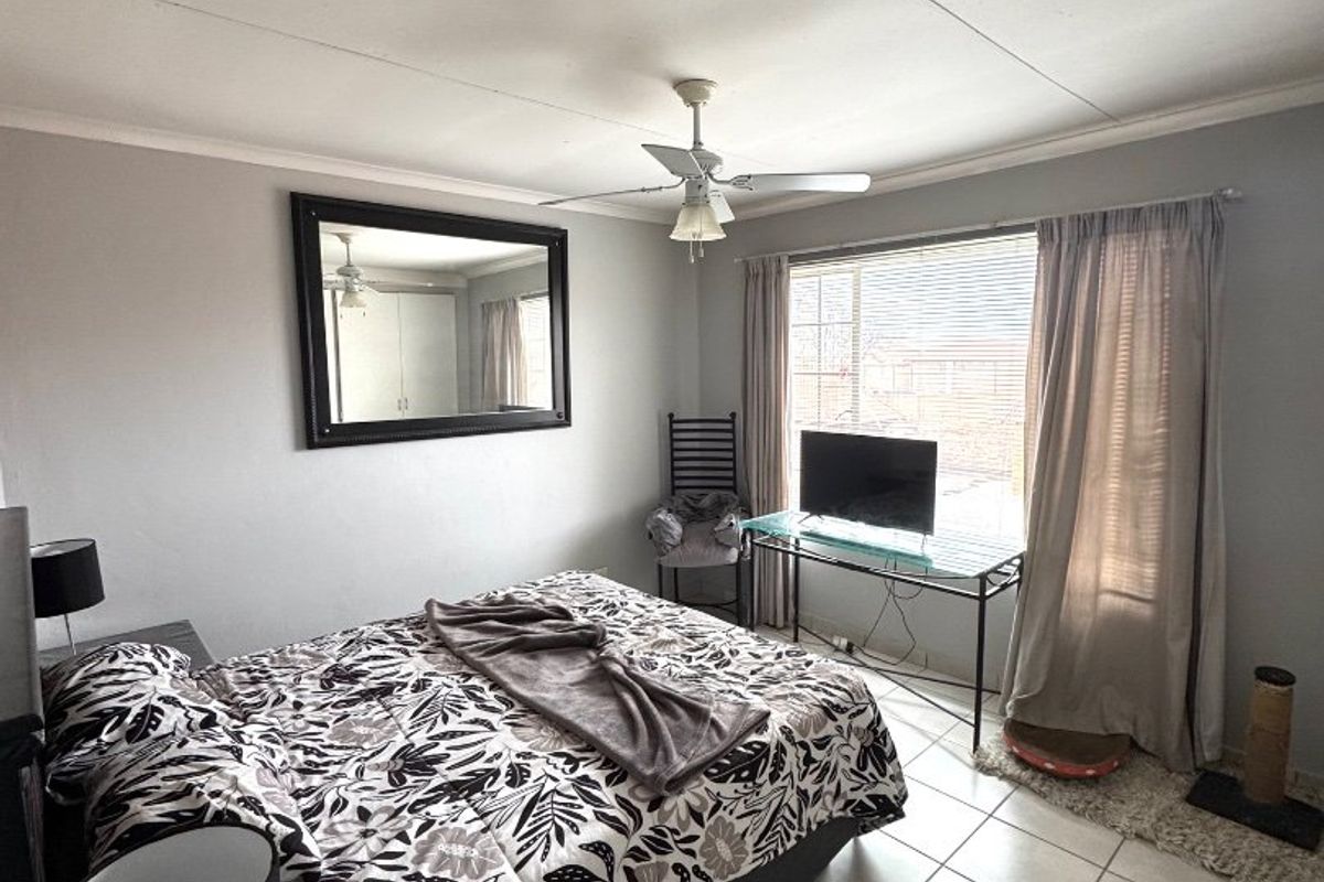 A bedroom featuring tiled flooring, a ceiling fan, and large windows with blinds, providing natural light.
