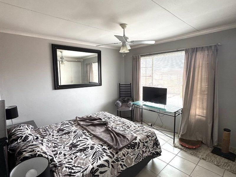 A bedroom featuring tiled flooring, a ceiling fan, and large windows with blinds, providing natural light.