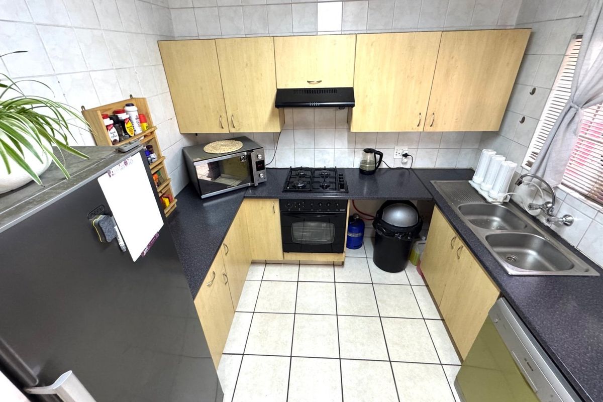 Functional kitchen featuring light wood-look cabinetry, dark laminate countertops, gas hob, built-in oven, and double stainless steel sink with tiled finishes.