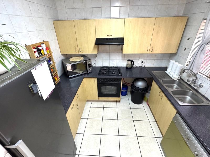 Functional kitchen featuring light wood-look cabinetry, dark laminate countertops, gas hob, built-in oven, and double stainless steel sink with tiled finishes.