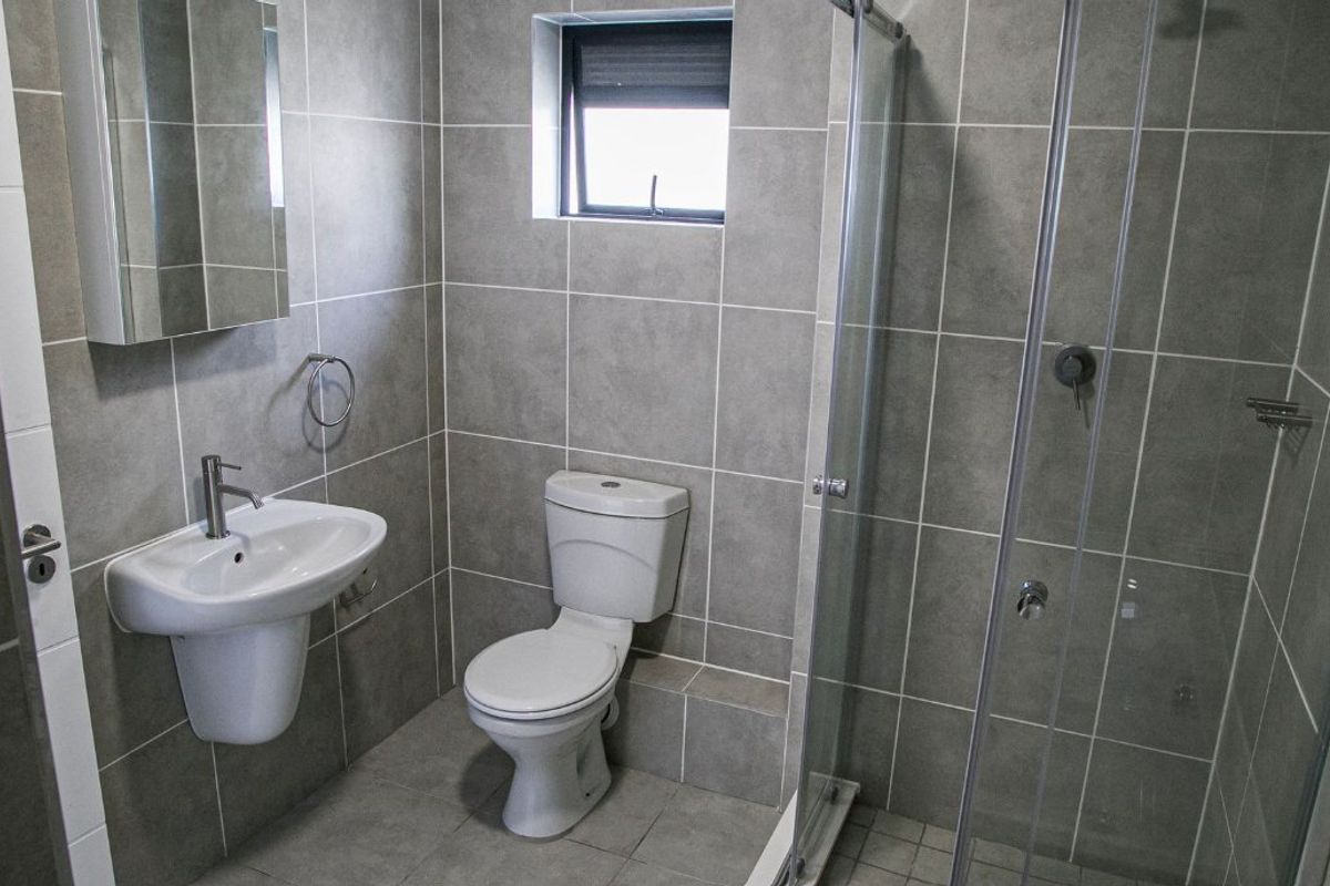 Modern bathroom featuring grey wall and floor tiles, a pedestal washbasin, a toilet, and a glass-enclosed shower.