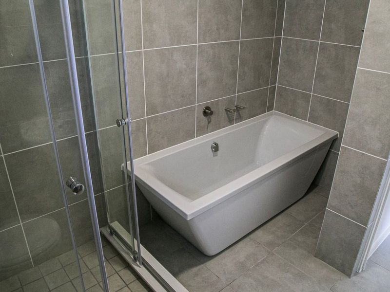 Modern bathroom featuring a sleek freestanding bathtub, a glass-enclosed shower, and contemporary grey ceramic tiling throughout.