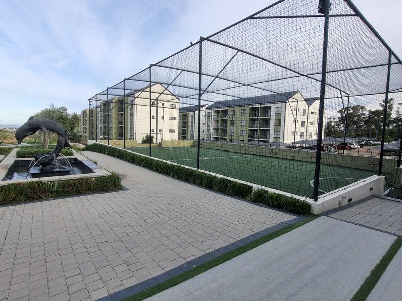 A well-maintained outdoor sports facility featuring an enclosed artificial turf court and a decorative water feature within the apartment complex grounds.