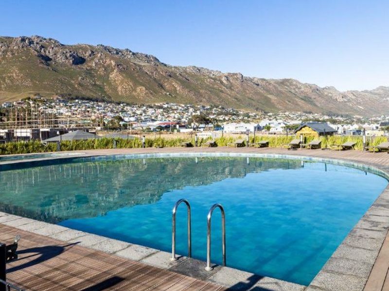 A well-maintained outdoor swimming pool area featuring timber decking, a pool ladder, and scenic mountain views in the background.