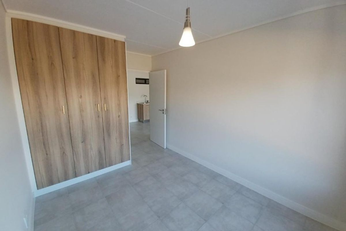 A clean, empty bedroom featuring modern wood-finish built-in cupboards, neutral tiled flooring, and a simple pendant light fixture.