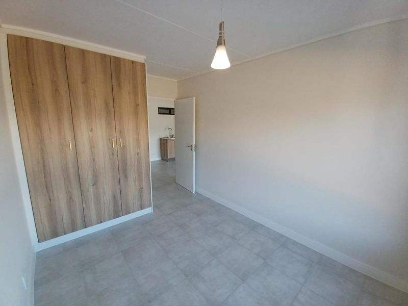 A clean, empty bedroom featuring modern wood-finish built-in cupboards, neutral tiled flooring, and a simple pendant light fixture.