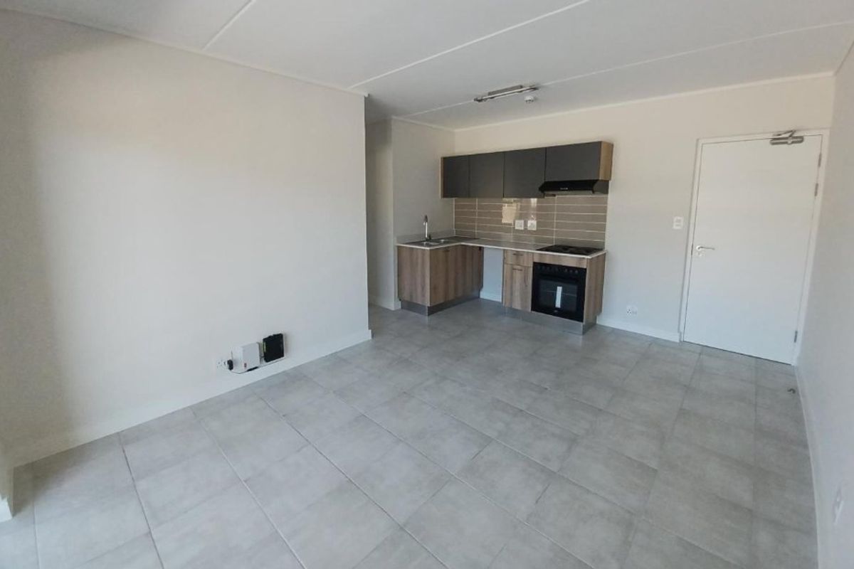 An open-plan living area featuring a modern kitchen with built-in cabinetry, integrated oven, hob, extractor fan, and neutral tiled flooring throughout.