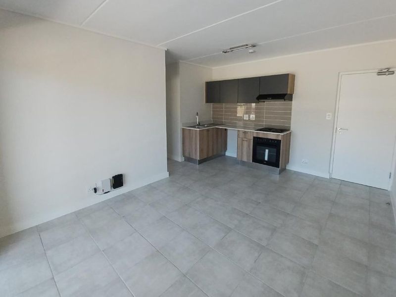 An open-plan living area featuring a modern kitchen with built-in cabinetry, integrated oven, hob, extractor fan, and neutral tiled flooring throughout.
