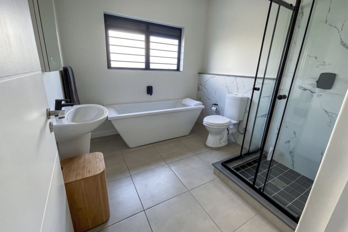 Modern bathroom featuring a freestanding bathtub, walk-in shower with black frame, pedestal basin, and contemporary marble-look wall tiling.