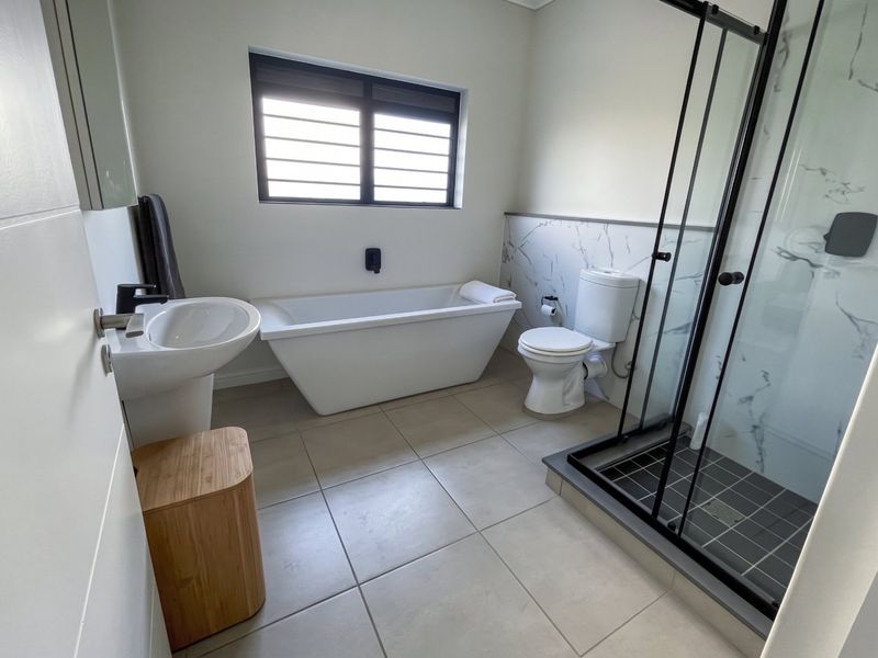 Modern bathroom featuring a freestanding bathtub, walk-in shower with black frame, pedestal basin, and contemporary marble-look wall tiling.