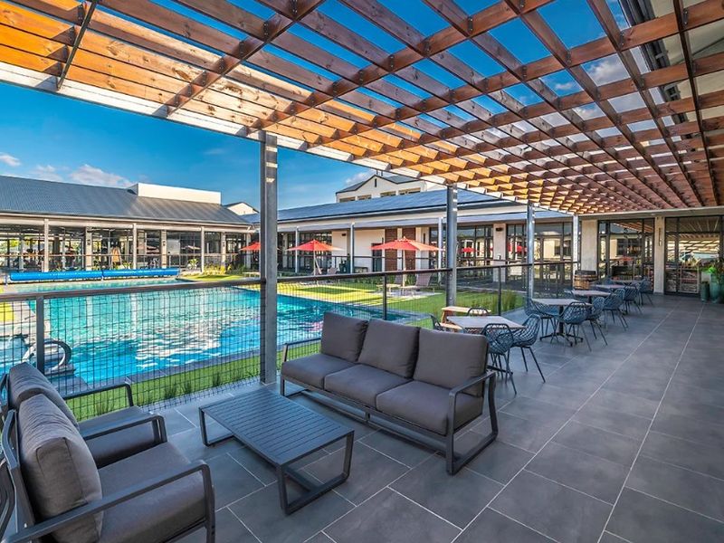 A well-maintained outdoor pool area featuring a large swimming pool, a spacious tiled patio, and a modern timber pergola for shade.